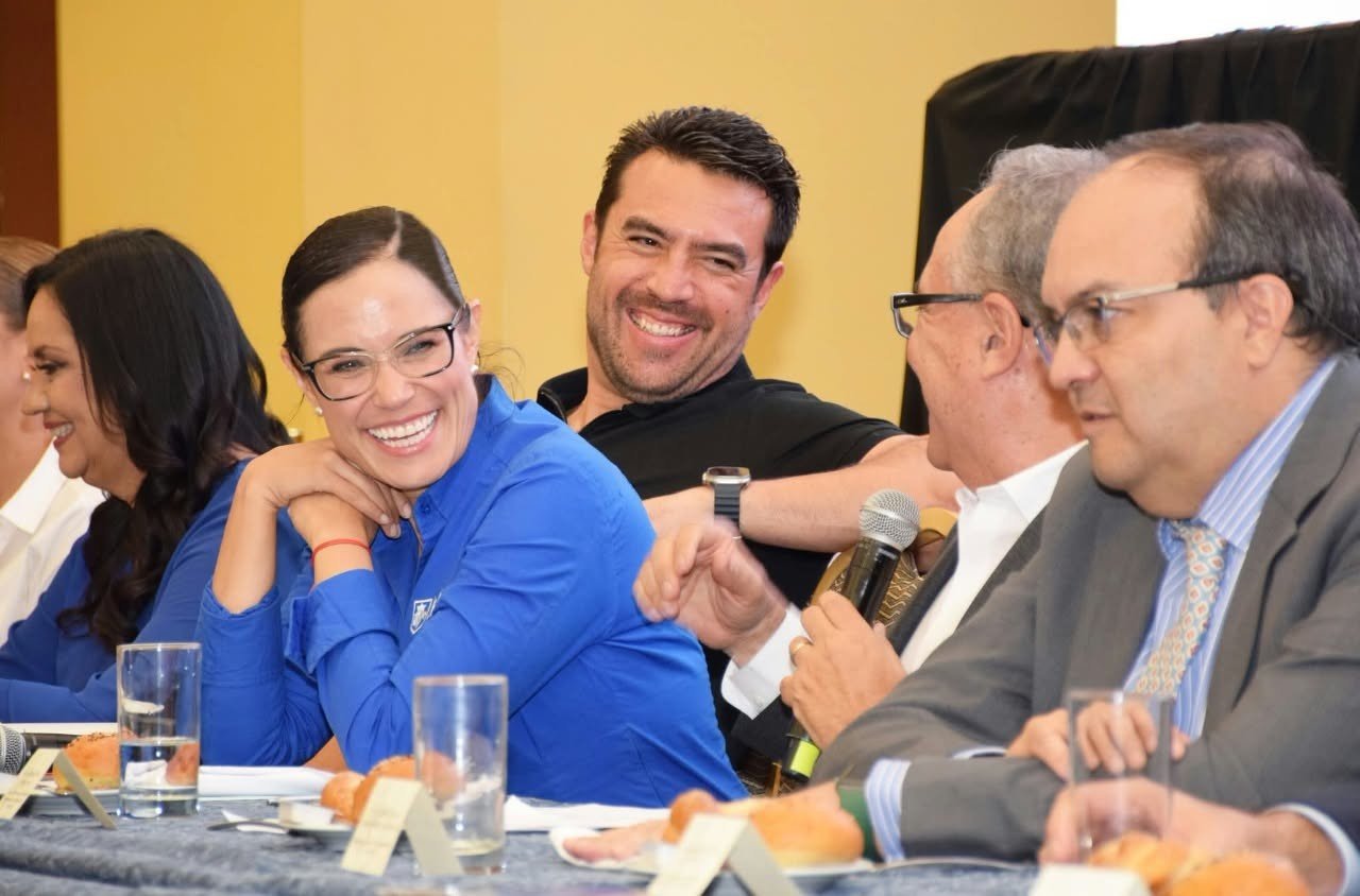 Asistentes a un desayuno de trabajo, sentados a una mesa con micrófonos.