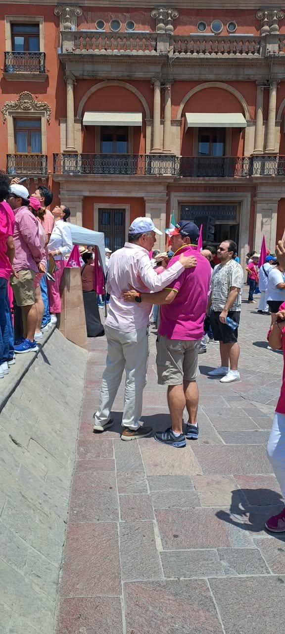 Personas con camisetas rosas en una plaza, frente a un edificio histórico.