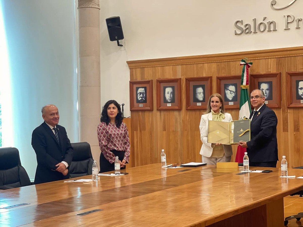 Cuatro personas en un salón con retratos enmarcados en la pared; dos de ellas son las exconsejeras del IEEG.