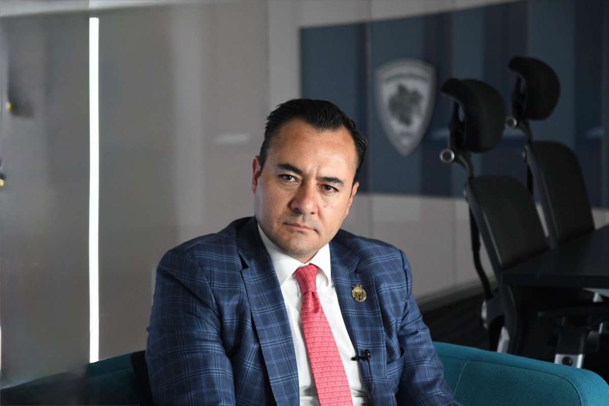 Retrato de Juan Mauro González Martínez, secretario de Seguridad y Paz de Guanajuato, sentado ante el escudo de la dependencia.