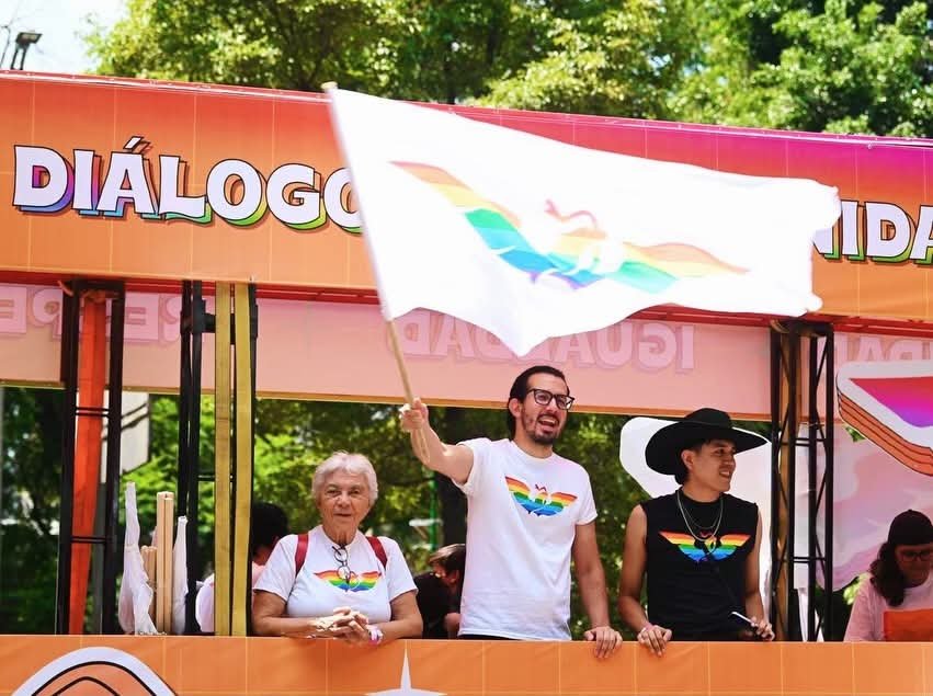 Juan Pablo Delgado ondea una bandera de Movimiento Ciudadano con los colores del arcoíris desde un carro alegórico