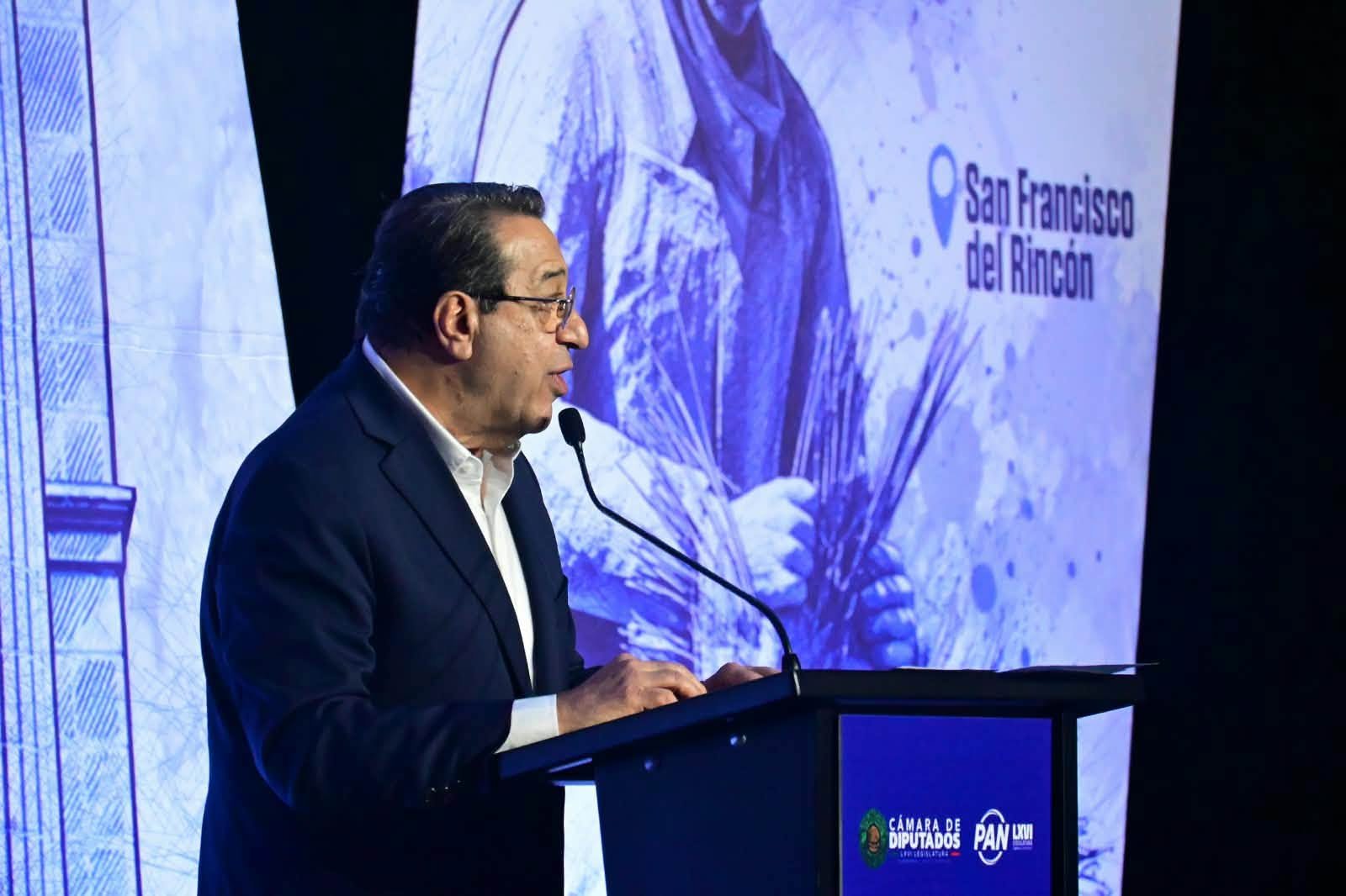 Un orador en el atril del informe, con un mural de San Francisco del Rincón al fondo.